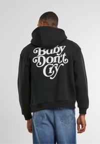 Zwarte hoodie met grote witte tekst "Baby Don’t Cry" op de rug. Gemaakt van zacht materiaal, met een ruime capuchon en geribde manchetten.