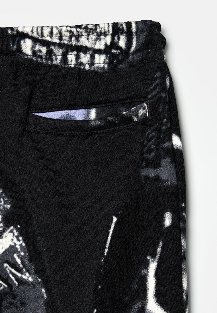 Schwarze Fleece-Jogginghosen mit einem einzigartigen schwarz-weißen Muster, einem elastischen Bund und einer kleinen mit Reißverschluss versehenen Tasche an der Seite.