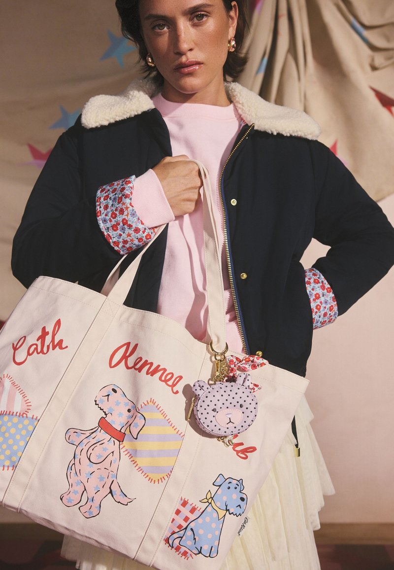 Tamsiai mėlynas švarkas su avies vilnos apykakle, rožinis džemperis ir smėlio spalvos rankinė su iliustruotais šunimis, raudonomis ir mėlynomis detalėmis bei gėlių ornamentais.