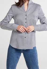 Krageklädd skjorta med svart och vit geometrisk mönstring, med långa ärmar och rak fåll, tillsammans med blå denimjeans.