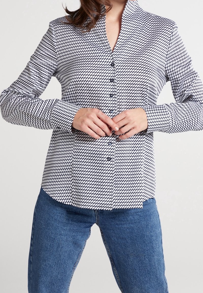 Krageklädd skjorta med svart och vit geometrisk mönstring, med långa ärmar och rak fåll, tillsammans med blå denimjeans.