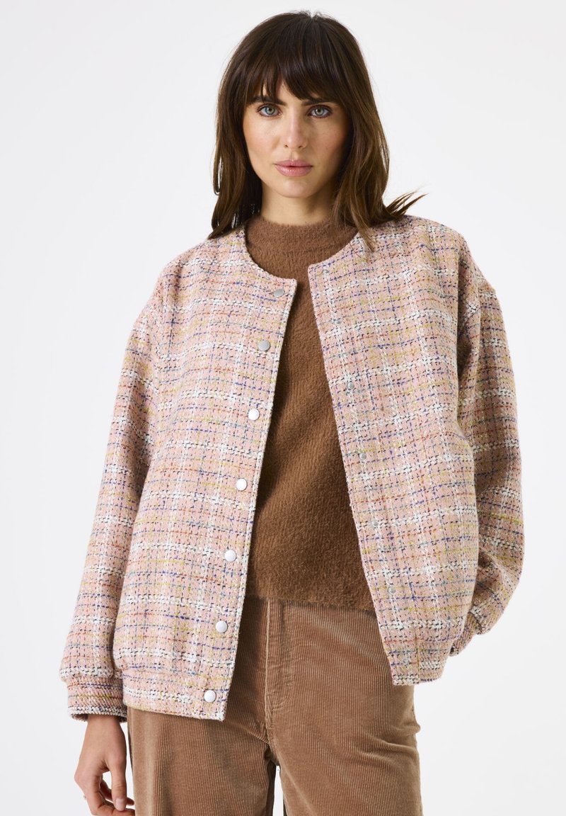 Tweed jasje in pastelroze, geel en wit; heeft een ronde halslijn, drukknoopjes en elastische manchetten. Gepaard met een bruine trui.