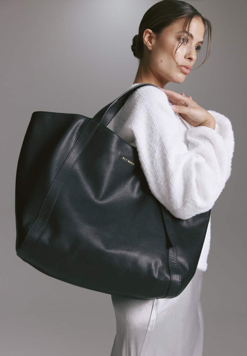 Grote zwarte leren tote bag met een gestructureerde afwerking, voorzien van twee stevige handvatten en een subtiele gouden logo aan de voorkant.