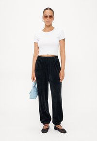 Hvit ripet crop-top, svarte fløyelsjoggebukser med elastiske mansjetter, og liten blå håndveske; modell iført tynne solbriller.