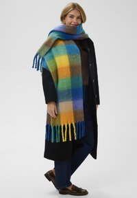 Uldent tørklæde i et livligt ternet mønster med blå, grønne, gule og orange nuancer. Frynser langs kanterne og blød tekstur øger varmen.