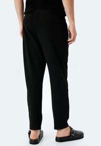 Svarta byxor med avslappnad passform, elastisk midja och två bakfickor. Matchar med svarta slip-on skor. Slät tygkvalitet.