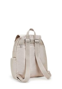Sac à dos en tissu beige avec double bandoulière, poignée supérieure et poche latérale. Présente un éclat subtil et des accents en métal argenté.