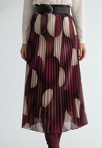 Plisowana spódnica z wzorem w bordowe, beżowe i brązowe koła, uzupełniona czarnym paskiem oraz gładkim, lejącym się materiałem.