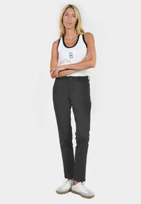 Zwarte slim-fit broek met een klassiek ontwerp, gecombineerd met een witte tanktop met een zwart logo, en witte sneakers met gumzolen.