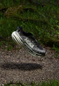 Mustaa ja harmaata trail-juoksukenkää, jossa on tekstuuripinta, kevyt välipohja ja suuri "HOKA"-logo sivussa.