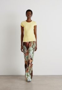 Yellow short-sleeve top with a fitted cut paired with brown floral print wide-leg pants featuring green and orange leaves.