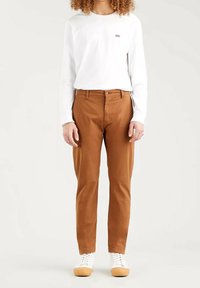 Bruna bomullsshorts med rak passform, med en knappstängning fram. I kombination med en vit långärmad skjorta och vita sneakers.