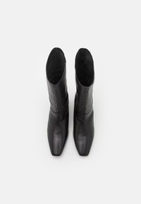 Botas de cuero negro hasta el tobillo con diseño de punta cuadrada, textura suave y silueta ajustada. El eje está ligeramente gathered en la parte superior.
