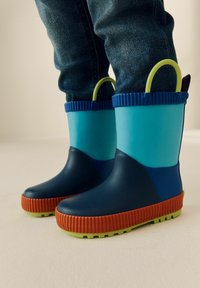 Bunte Gummistiefel in Blau und Marineblau mit einer strukturierten orangefarbenen Sohle und grünen Akzenten. Beinhaltet eine gerippte Oberseite und einen Griff.