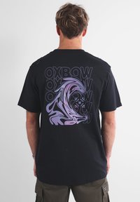 T-shirt in cotone nero con una grande grafica a onde viola e bianche e un design di testo ripetuto sul retro. Maniche corte e scollatura rotonda.