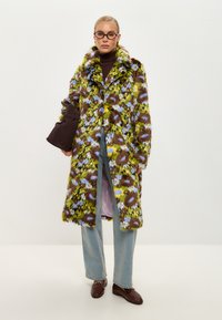 Palton din blană sintetică multicolor, cu un model floral în nuanțe de verde, maro și albastru, având un guler mare și mâneci lungi. Asortat cu blugi.