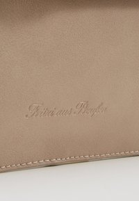 Beige Lederaccessoire mit strukturierter Oberfläche, versehen mit geprägten Buchstaben. Genähte Kanten verleihen dem Gesamtdesign zusätzliche Details.