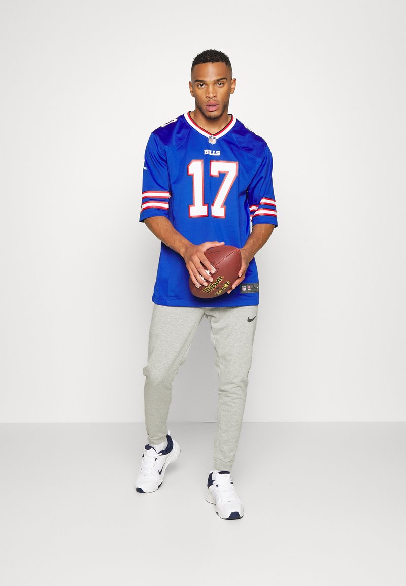Camisa de futebol de manga curta azul com "BILLS" e "17" em branco e laranja. Calças de jogging justas cinzas. Ténis brancos com detalhes em azul-marinho.
