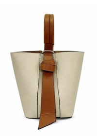 Sac seau en cuir crème avec une anse et des détails de bandoulière en cuir tan. Présente une texture lisse et un design minimaliste.