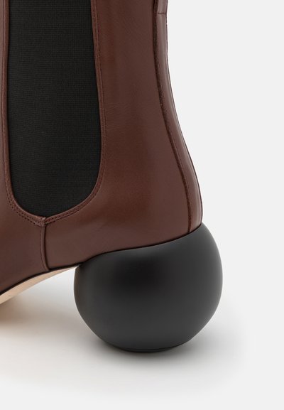 Bottine en cuir marron avec un panneau élastique noir et un talon noir arrondi. Texture lisse avec un design solide pour la stabilité.