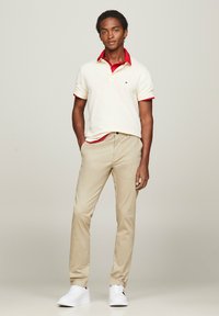 Polo crema con dettagli rossi al colletto, chinos color beige e sneaker bianche. Il polo ha maniche corte e un piccolo logo sul petto.