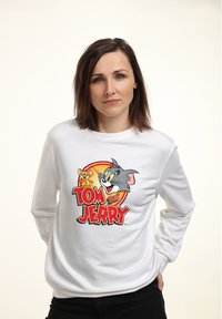 Bílá mikina s velkým, barevným potiskem Toma a Jerryho na oranžovém kruhovém pozadí. Měkká tkanina, dlouhé rukávy, volný střih.