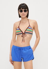 Prugasti krošej bikini top u više boja s smešnim obrubom i vezicama; upareno s plavim kupaćim šortsevima s elastičnim strukom i džepovima.