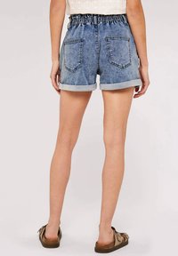 Denim-Shorts mit umgeschlagenem Saum, elastischem Bund und zwei Gesäßtaschen. Der Stoff ist mittelblau mit verwaschenen Stellen und leichtem Strukturmuster.