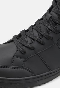 Black leather high-top sneaker with textured surface, flat black laces, and reinforced toe. Features subtle stitching and rubber sole.