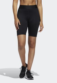 Shorts de sport noirs avec une taille haute, une texture lisse et une coupe ajustée, s'étendant jusqu'à mi-cuisse, associés à des chaussures de course noires.