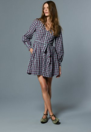 Geruit jurkje met lange mouwen, een getailleerde taille met riem en zijzakken. Kleuren zijn diep rood en blauw. Zachte stof in een speels fit-and-flare ontwerp.
