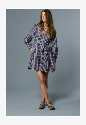 Robe à carreaux avec manches longues, taille ceinturée et poches latérales. Couleurs comprenant un rouge profond et du bleu. Tissu doux avec une coupe évasée ludique.