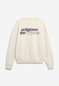 Sweat-shirt couleur crème avec une coupe décontractée, poignets et ourlet côtelés. Présente le texte "outgrown the system" imprimé en bleu marine foncé.