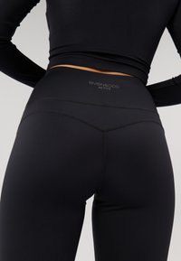 Schwarze aktive Leggings mit einem hohen Bund, die auf der Rückseite ein Logo und dezente Nahtdetails für ein elegantes Erscheinungsbild aufweisen.