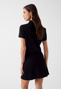 Czarna sukienka z krótkim rękawem, z dopasowanym gorsetem i rozkloszowaną spódnicą, wykonana z gładkiego materiału. Posiada kołnierzyk i ozdoby z tyłu.