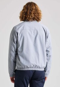 Hellgraue Bomberjacke aus glattem Material, mit einem gerippten Saum, Bündchen und einem schlichten Design ohne sichtbare Muster oder Akzente.