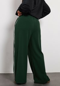 Gröna vida byxor i en mjuk textur, med en vit sidstripe och ett elastiskt midjeband. Bärs med en svart långärmad topp.