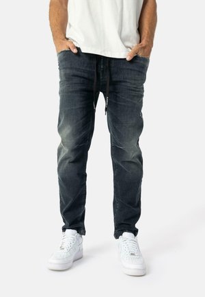 Mørkeblå denim jeans med en falmet finish, der har en snor i taljen, sidelommer og en afslappet lige benpasform. Sammen med hvide sneakers.