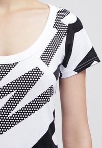 Černobílá tričko s krátkým rukávem s geometrickým vzorem a puntíky, s kulatým výstřihem a hladkým bavlněným povrchem.