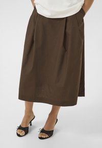 Pruun voltidega seelik kerge materjaliga, põlvepikkune, küljetaskute ja siledaga. Sobitunud mustade avatud varvaste kontsakingadega.