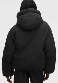 Sort polstret jakke med en stor hætte, buede sømme og oversized pasform. Glat tekstur med volumens form og elastisk kant.