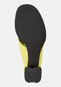 Scarpa di stoffa gialla con una suola in gomma nera liscia, caratterizzata da un motivo testurizzato e un'accortezza rettangolare sul tacco.