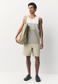 T-krekls ar baltām un bēšām horizontālām svītrām, bēšas šorti un tumši brūnas slip-on kurpes; nēsā lielu bēšu somu ar logotipu.