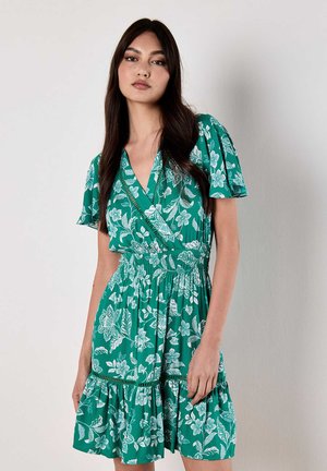 Groene wikkeljurk met witte bloemenpatronen, korte mouwen, gesmokt taille en gerimpelde zoom. Lichtgewicht stof, casual ontwerp.