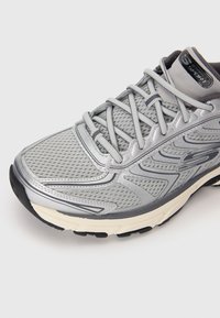 Gray Skechers running shoe with mesh upper, detailed stitching, gray laces, and black and beige sole on white background.