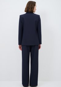 Mörkblå kostym med en skräddarsydd jacka och byxor med vida ben, tillverkad av ett mjukt tyg. Inga synliga mönster eller detaljer.