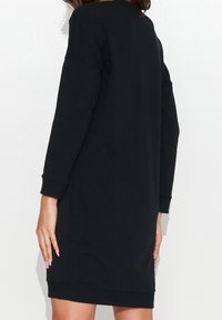 Schwarzes Sweatshirtkleid mit langen Ärmeln, lockerer Passform, abgerundetem Saum und gerippten Bündchen. Glattes Material ohne sichtbare Muster oder Akzente.