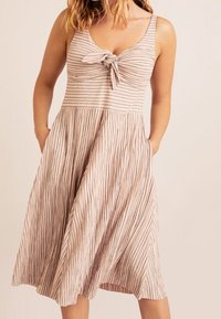 Vestido midi a rayas de color rosa claro con detalle de nudo en la parte delantera, tirantes finos y bolsillos laterales, que presenta una textura de falda plisada.