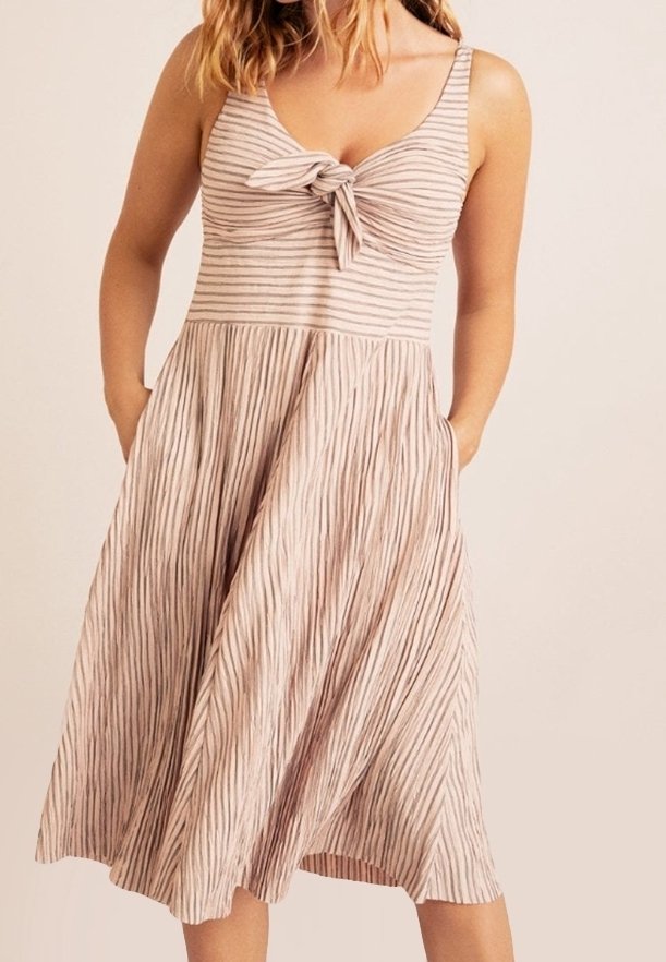 Vestido midi a rayas de color rosa claro con detalle de nudo en la parte delantera, tirantes finos y bolsillos laterales, que presenta una textura de falda plisada.