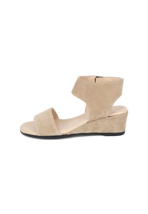 Beige Wildleder Keilsandalette mit Knöchelriemen und offenem Zeh, niedrigem Absatz und schwarzer Sohle auf weißem Hintergrund.